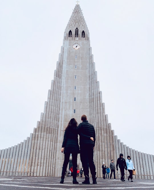 people walking on gray concrete pathway near gray concrete building during daytime in Hallgrimskirkja Iceland