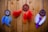 Three dreamcatchers with colorful feathers hang against a wooden wall backdrop. The left dreamcatcher features blue feathers and a central blue bead. The middle one has vibrant red and orange feathers with a decorative icon in the center. The right piece displays purple and white feathers with a central purple embellishment.
