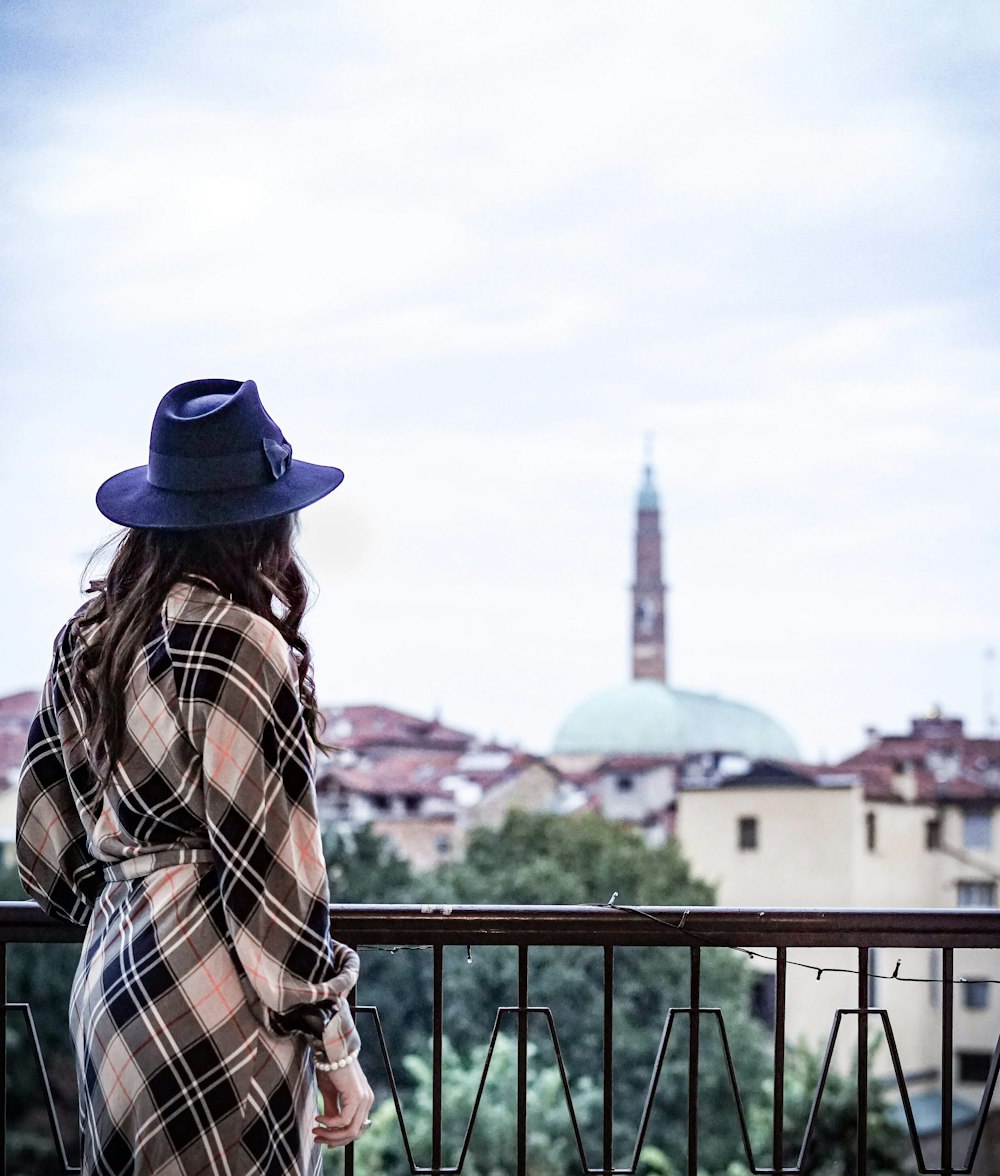 man in brown white and black plaid dress shirt and blue fedora hat standing near railings