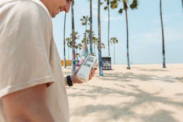 A person carrying a delivery box along a sandy beach with waves gently crashing nearby.