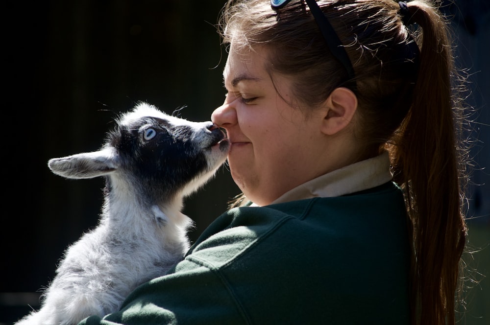 woman in green jacket holding white and black dog