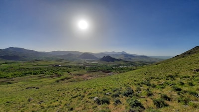 A serene landscape of rolling hills and distant mountains under a bright blue sky.