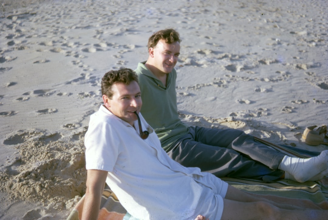 man in white shirt and black pants sitting on gray sand during daytime