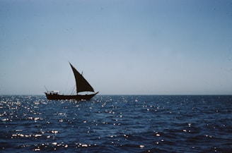 black sail boat on sea under gray sky