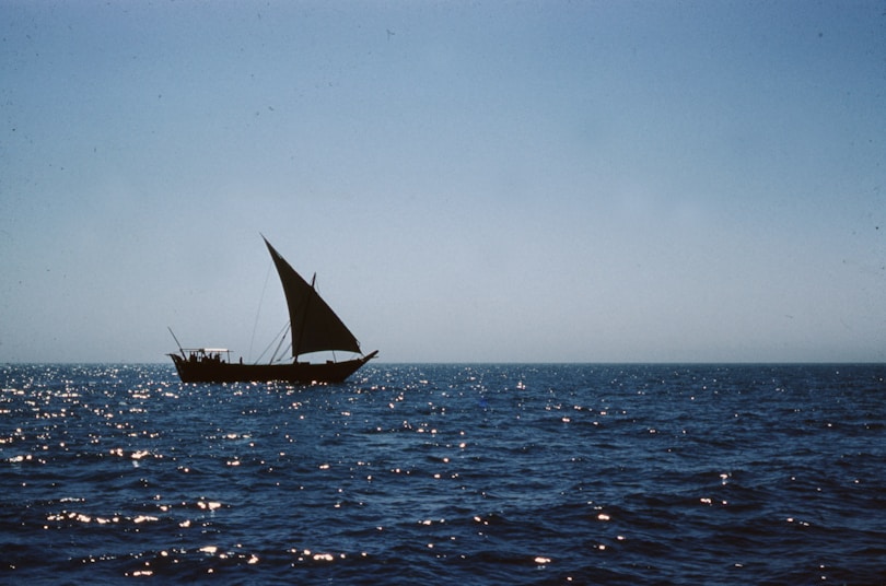 black sail boat on sea under gray sky