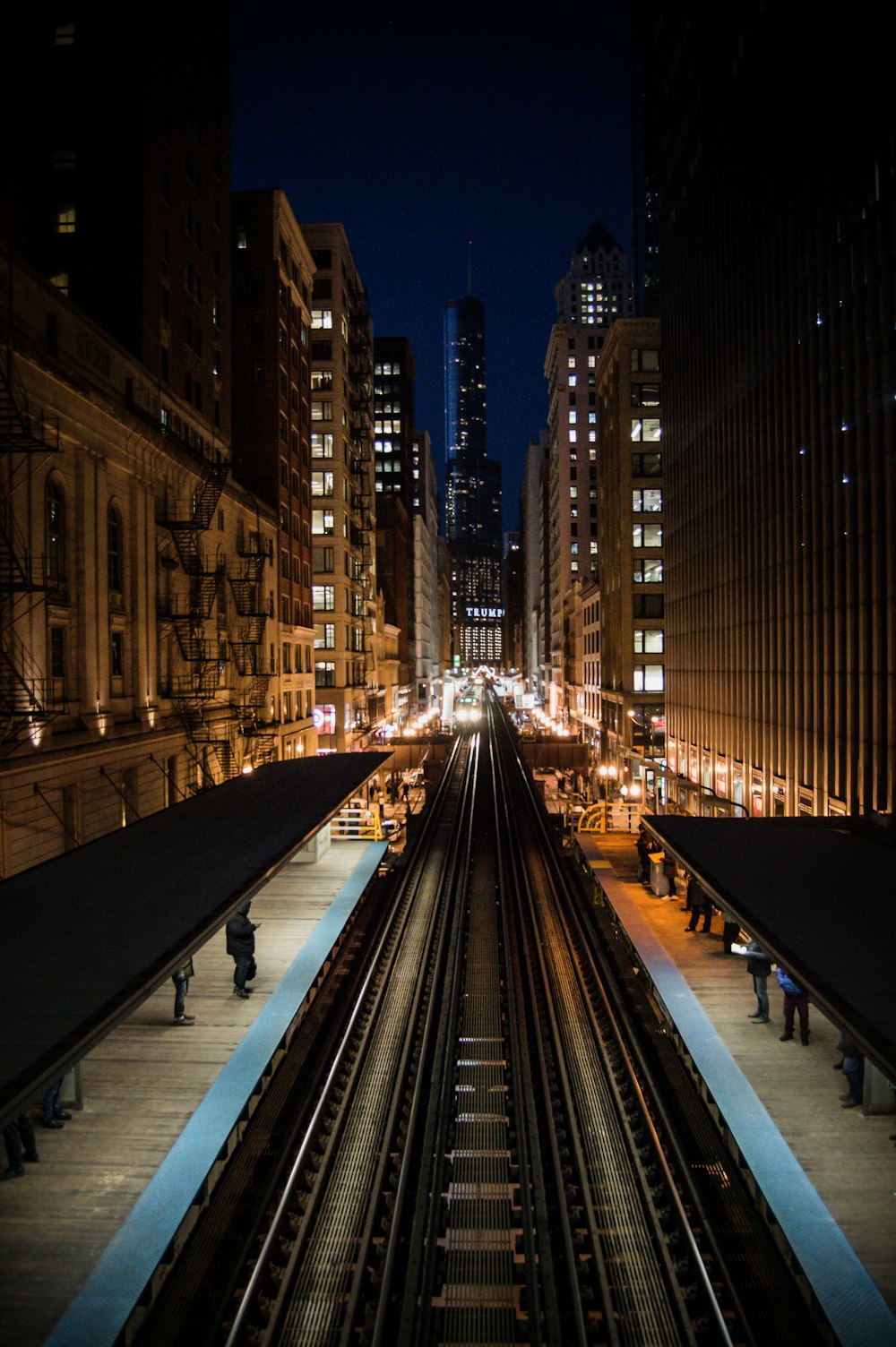 black metal train rail in between high rise buildings during night time