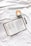 A book is laid open on a white fabric surface next to a cappuccino in a light green cup. Beside the book is a black pen. The book appears to be a Bible open to the Book of Jonah.