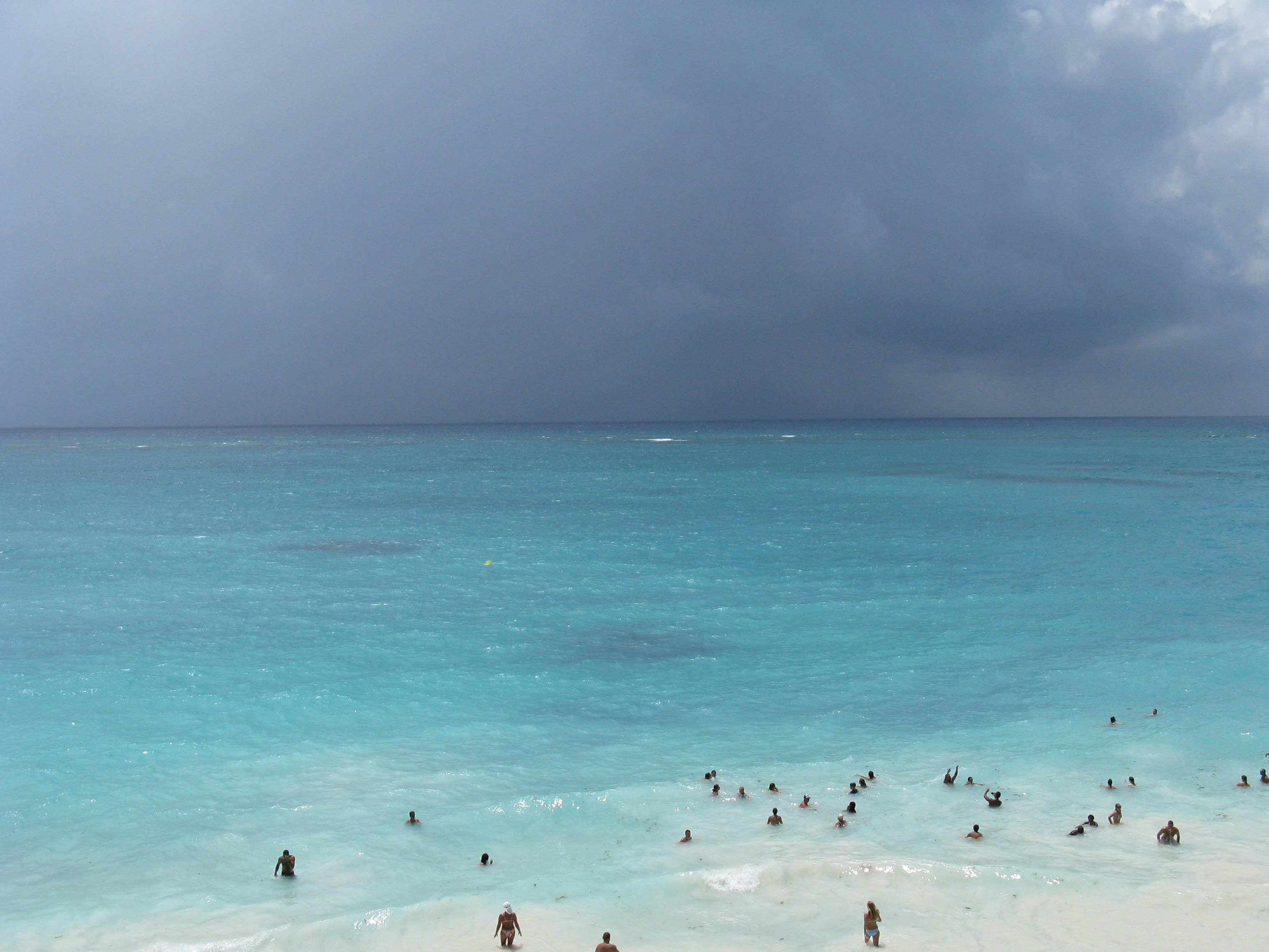 people on beach during daytime, people in the turquoise ocean in spite of a brewing storm