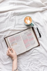 person holding white book page beside black pen on white textile