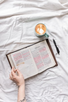 person holding white book page beside black pen on white textile