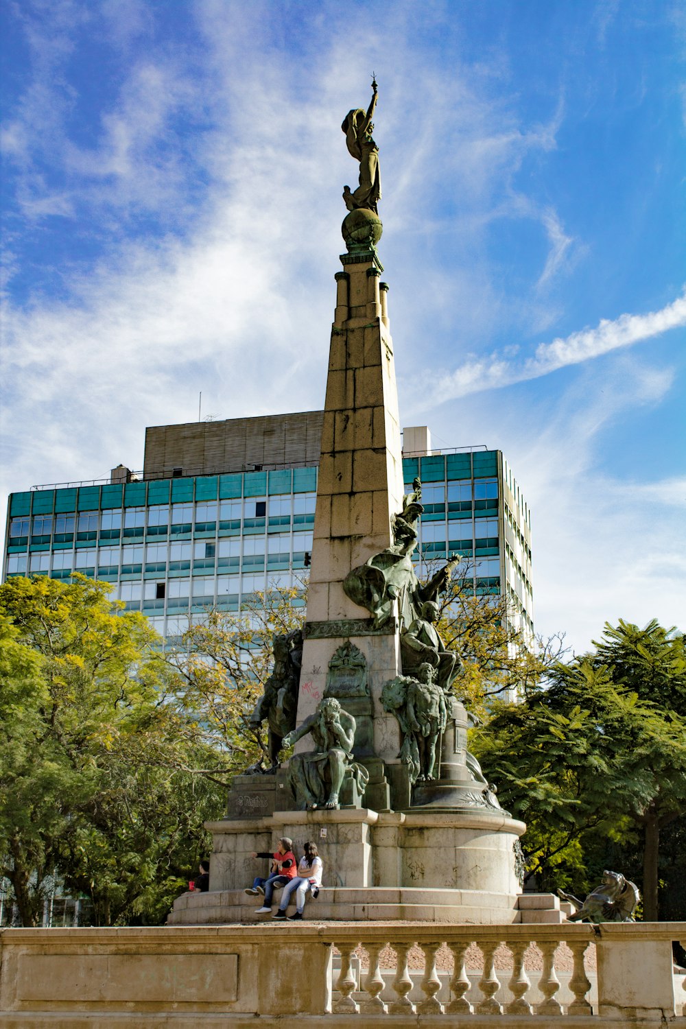 Statua di cemento grigio vicino agli alberi verdi e alla costruzione durante il giorno