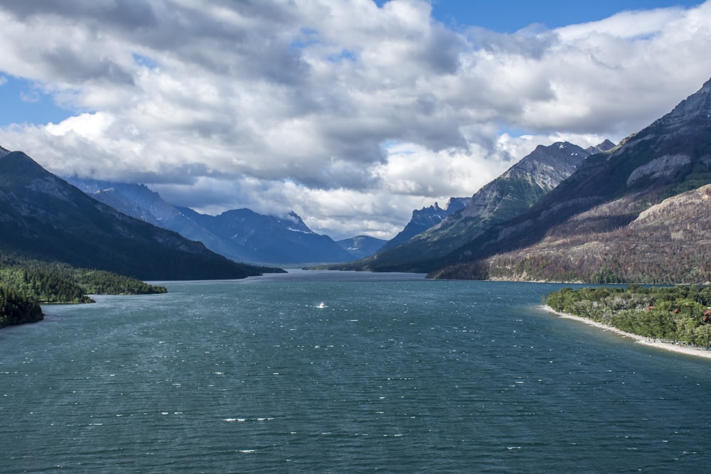 green lake near mountain under white clouds and blue sky during daytime