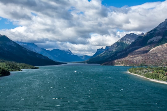 green lake near mountain under white clouds and blue sky during daytime in Waterton Lakes National Park of Canada Canada