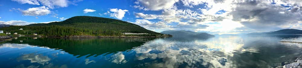 green mountain beside body of water under blue sky and white clouds during daytime