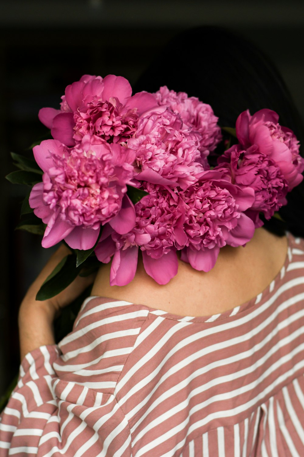 Mujer con camisa de rayas blancas y rojas sosteniendo una flor rosa