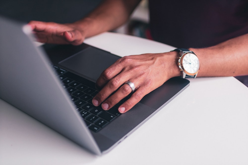 person wearing gold analog watch using black laptop computer