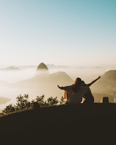 man in brown jacket sitting on concrete fence during daytime