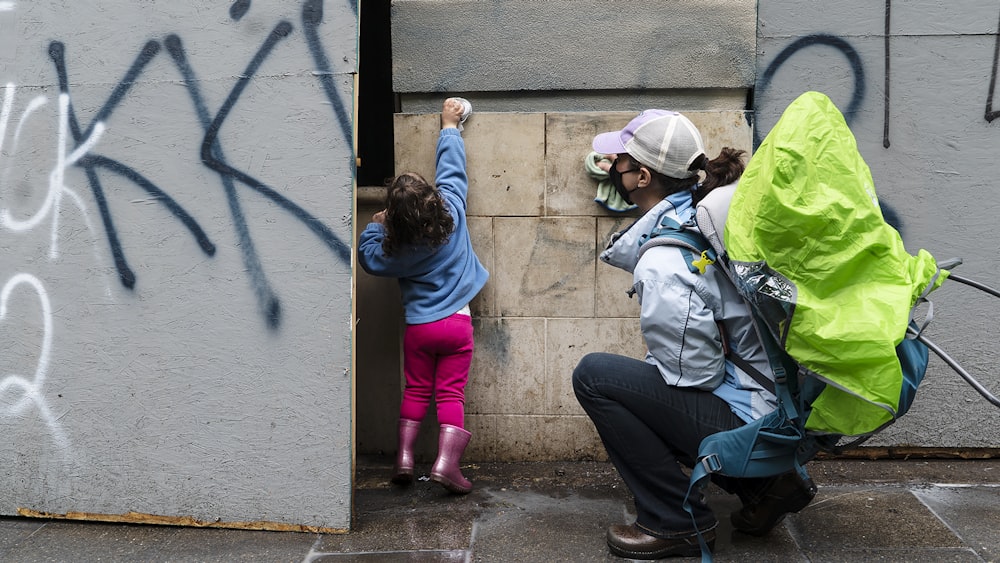 2 children in blue and green jacket and blue denim jeans sitting on concrete floor during