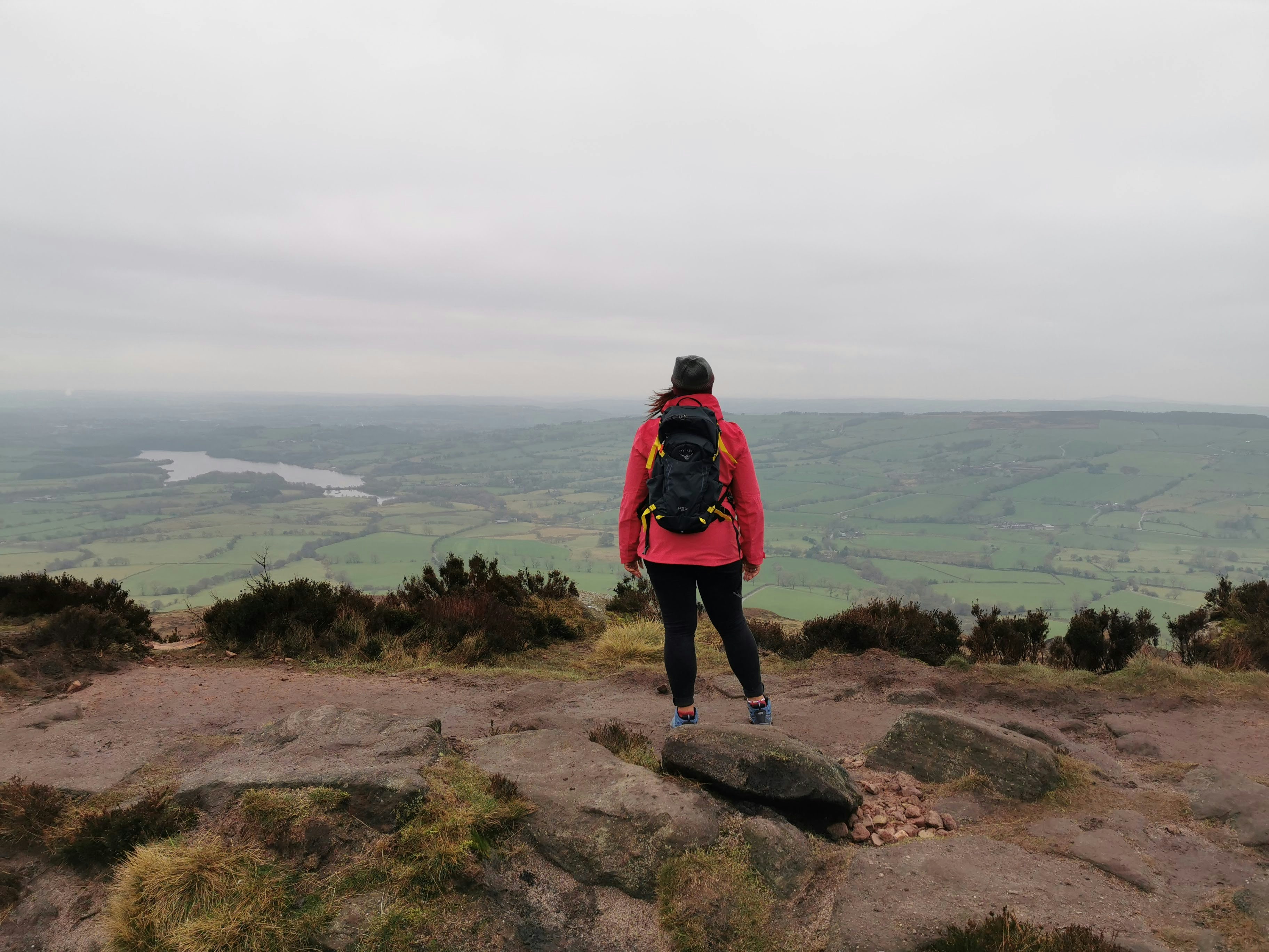 man in black and red jacket standing on rock formation looking at the sea during daytime