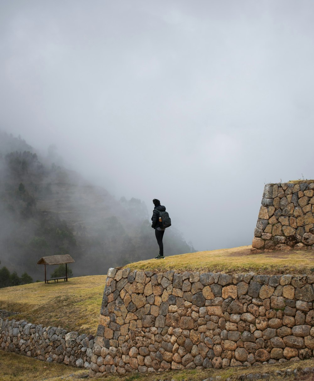 person in black jacket standing on rock formation during foggy weather