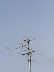 A collection of various ham radio antennas set up outdoors against a clear blue sky.