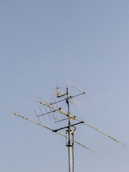 A complex array of metal antennas with various sections and angles mounted on a tall pole against a clear blue sky.
