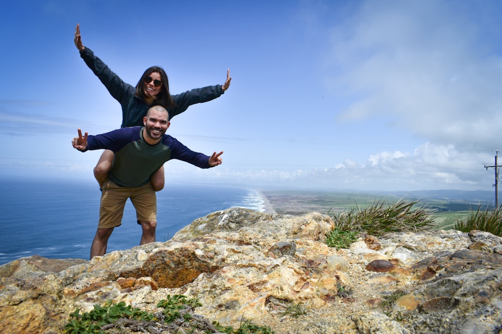 man in blue shirt and brown shorts standing on rock formation during daytime