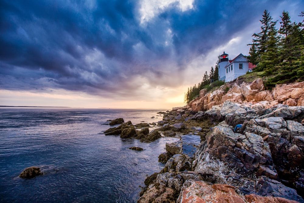 white and red concrete house on rocky shore under blue sky during daytime