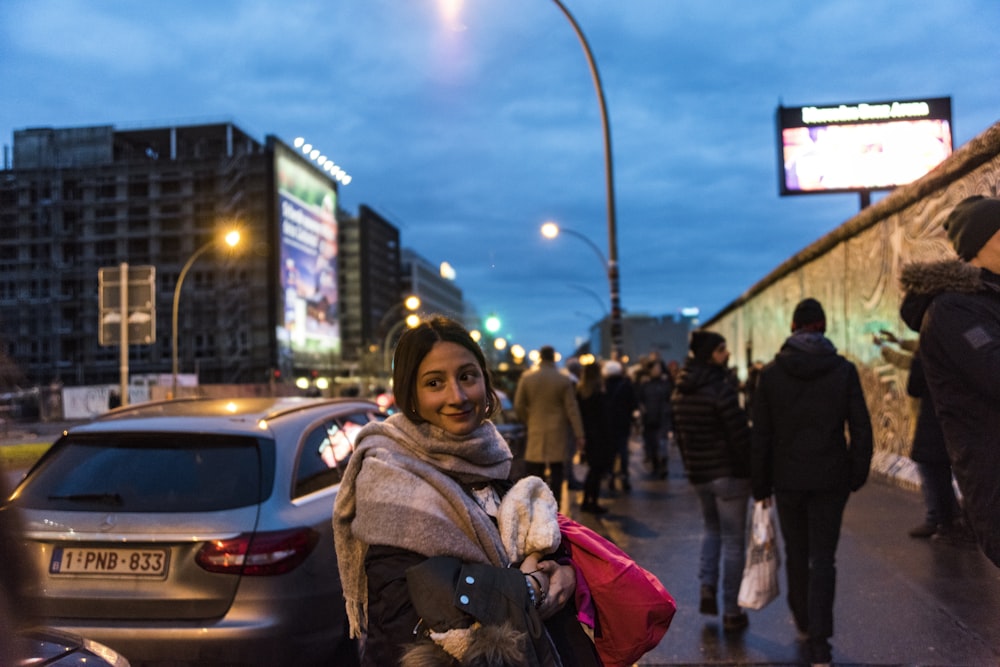 woman in brown coat standing near white car during night time