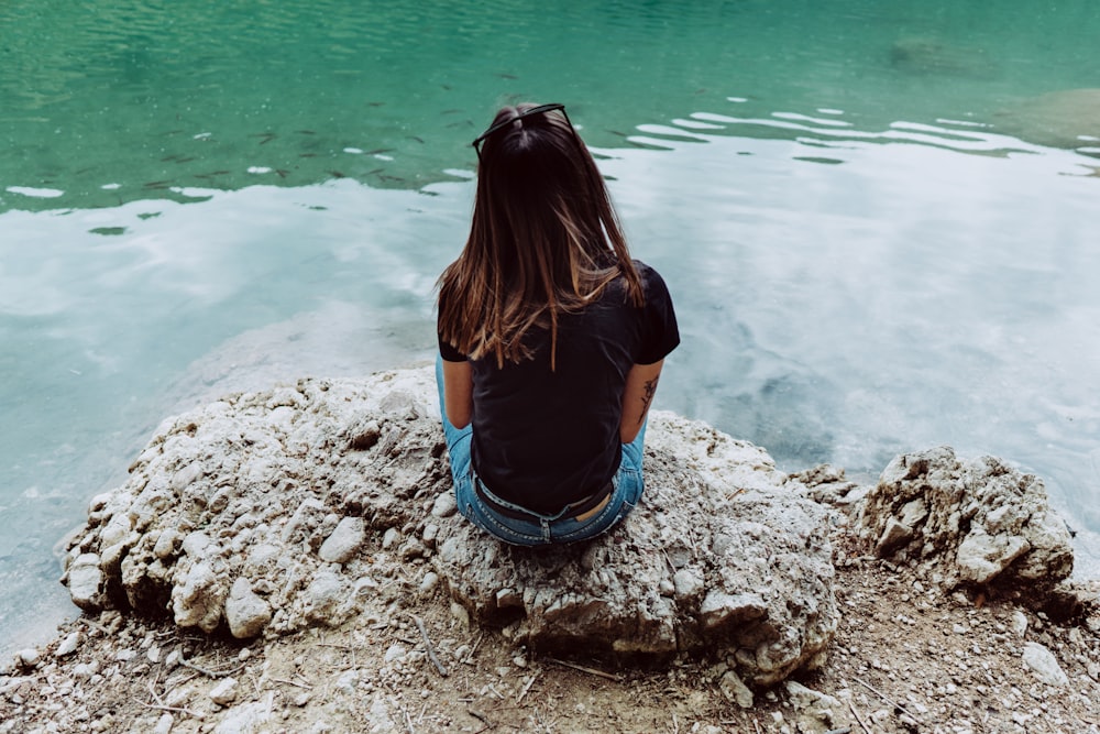 woman in blue shirt and blue denim shorts sitting on rock by the sea during daytime