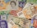 A collection of various international currency notes is spread out. The notes include representations of people and intricate designs. Different denominations are visible, showcasing a variety of currencies including pounds, dollars, and Euros.