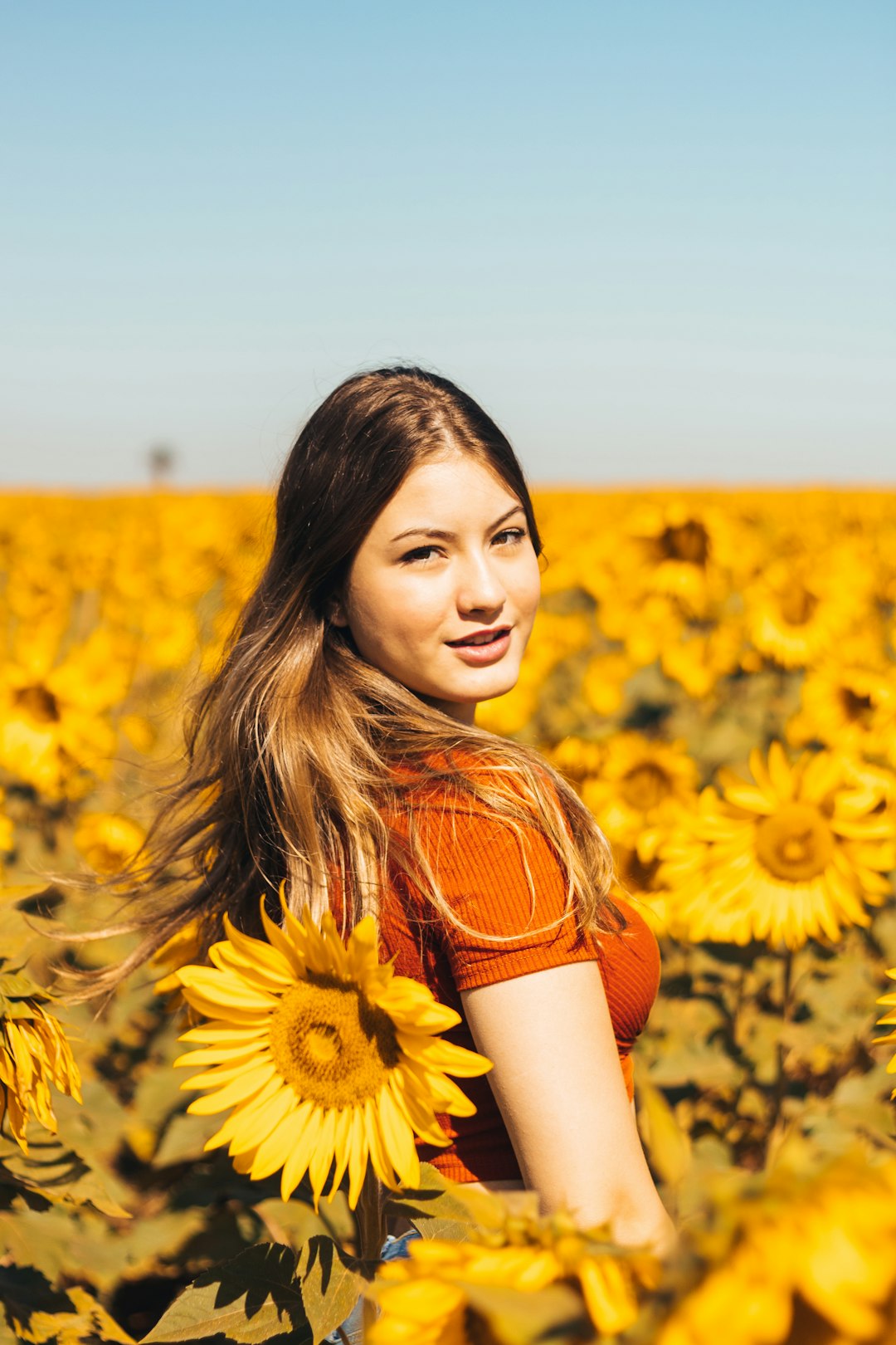 woman in orange and white stripe shirt standing on sunflower field during daytime