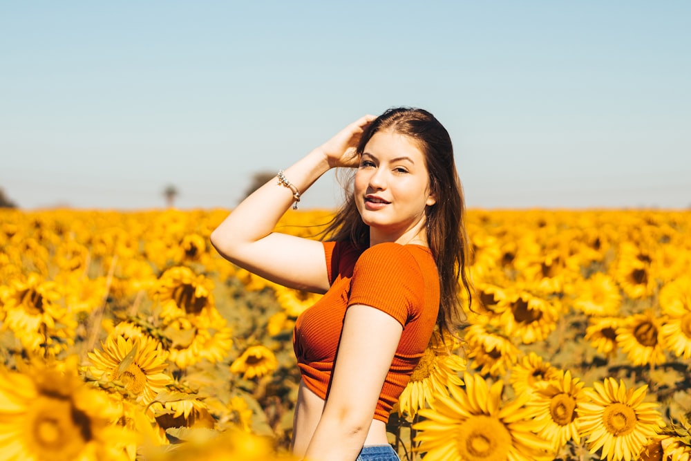 woman in orange tank top standing on sunflower field during daytime