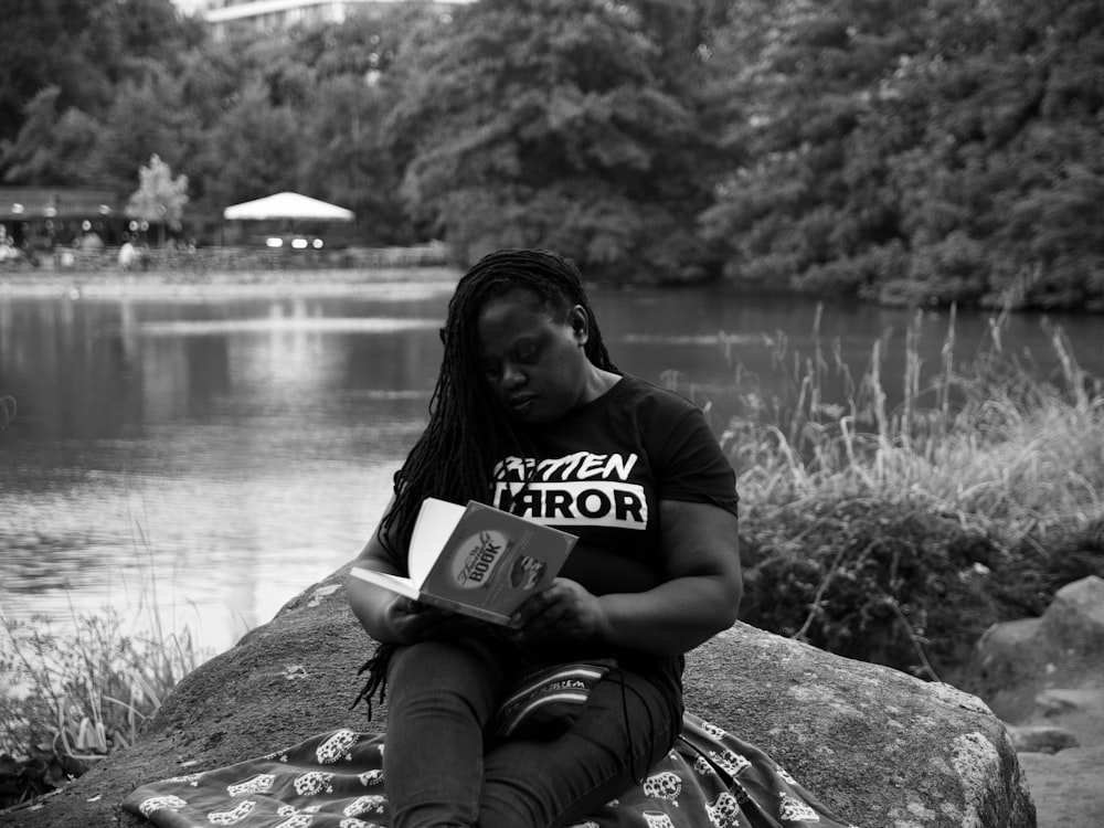 man in black t-shirt sitting on rock near body of water