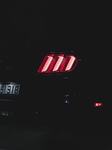 The image features the rear lights of a car glowing brightly in a dark background. The taillight design includes three vertical red bars. A part of the license plate, displaying the numbers 91918, is also visible on the left side.