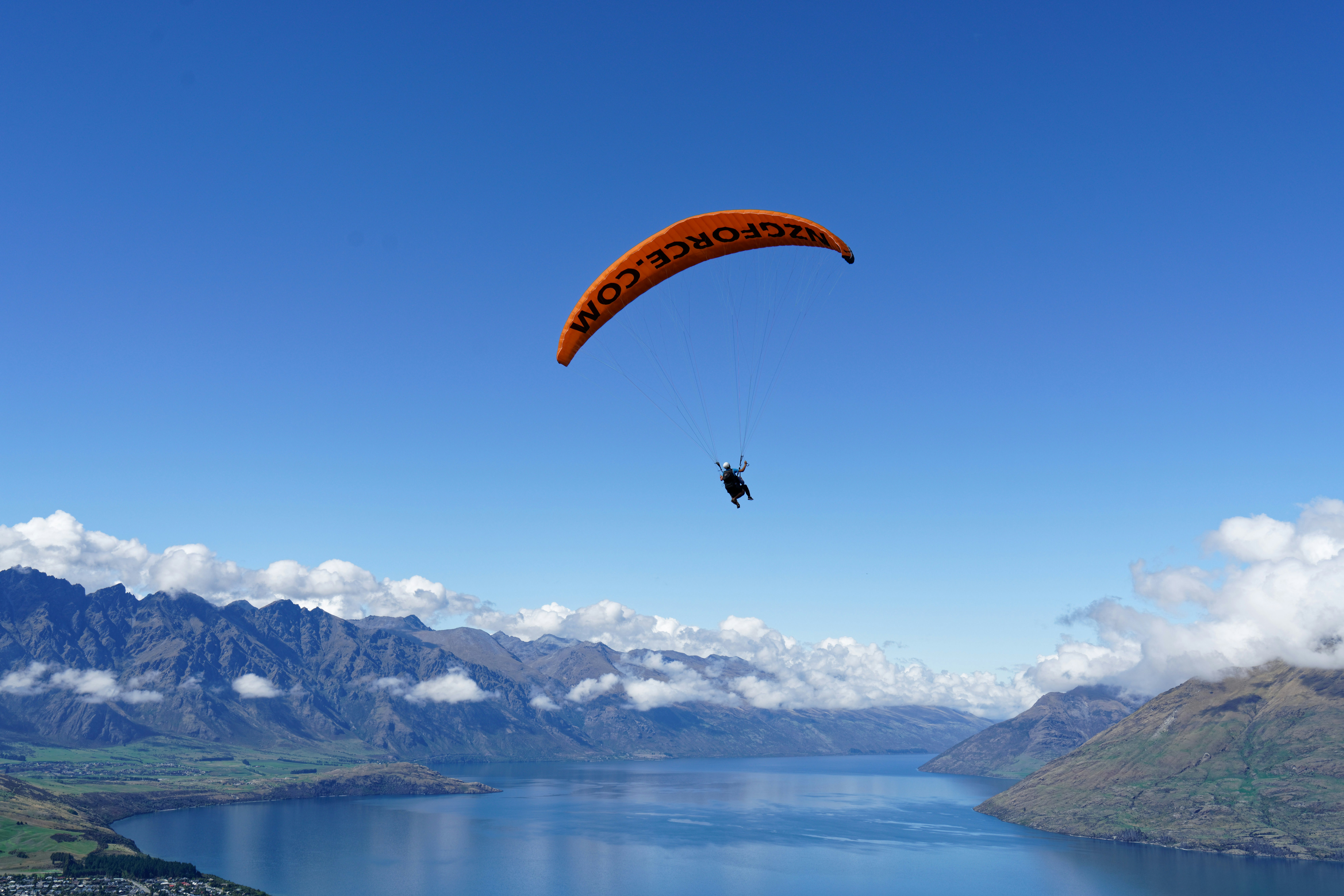person in parachute over snow covered mountains during daytime, Paragliding over Queens Town on the South Island of New Zealand