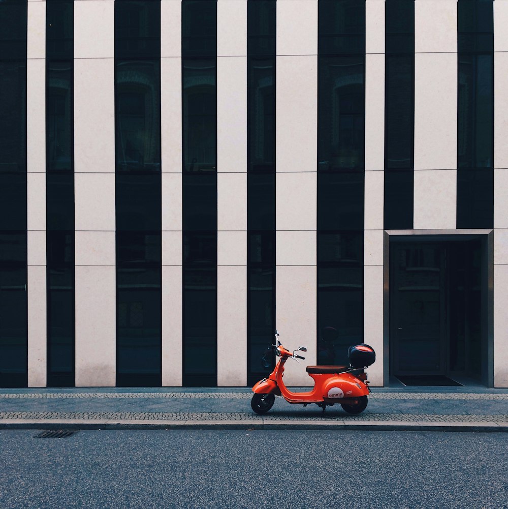 Scooter naranja y negro estacionado junto a un edificio de concreto blanco y gris durante el día