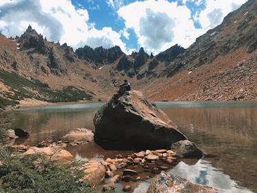 A quiet moment of reflection beside a mountain lake, where a traveler in their late 50s gazes thoughtfully at the horizon.