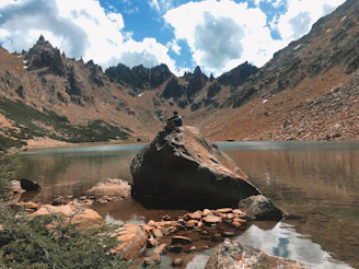 A quiet moment of reflection beside a mountain lake, where a traveler in their late 50s gazes thoughtfully at the horizon.