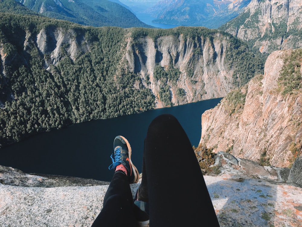 person in black pants and blue sneakers sitting on rock