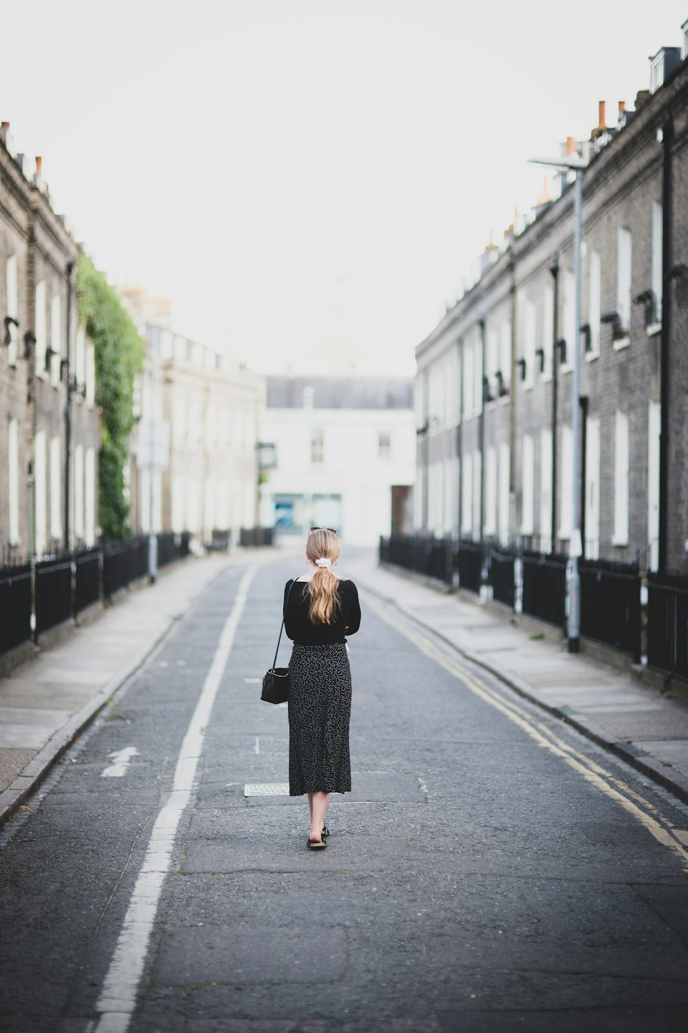 woman in black coat standing on road during daytime