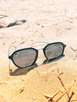 A stylish pair of sunglasses resting on a summer beach towel with sunlight reflections.