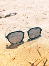 Sunlight catching on elegant sunglasses placed on a beach towel by the ocean.