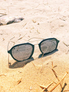Sunlight reflecting off trendy sunglasses on a beach towel by the ocean.
