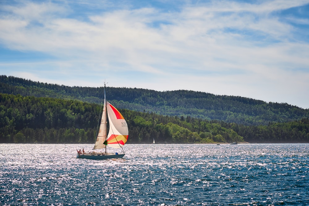 white sailboat on sea near green trees under white clouds during daytime