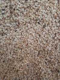 A close-up of a large quantity of sesame seeds densely packed together. The seeds are small, oval, and have a pale beige color with slight variations in tone.