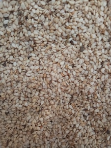 A close-up of a large quantity of sesame seeds densely packed together. The seeds are small, oval, and have a pale beige color with slight variations in tone.