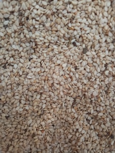 A close-up of a large quantity of sesame seeds densely packed together. The seeds are small, oval, and have a pale beige color with slight variations in tone.
