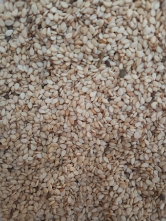 Close-up of natural sesame seeds spilling from a burlap sack on a clean white surface.