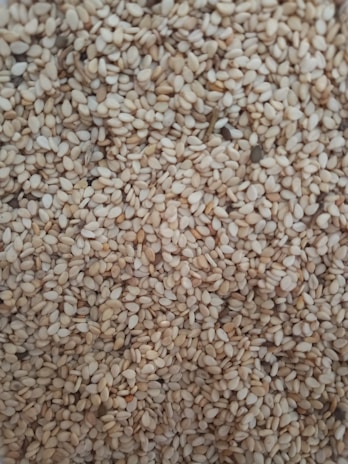 A close-up of a large quantity of sesame seeds densely packed together. The seeds are small, oval, and have a pale beige color with slight variations in tone.